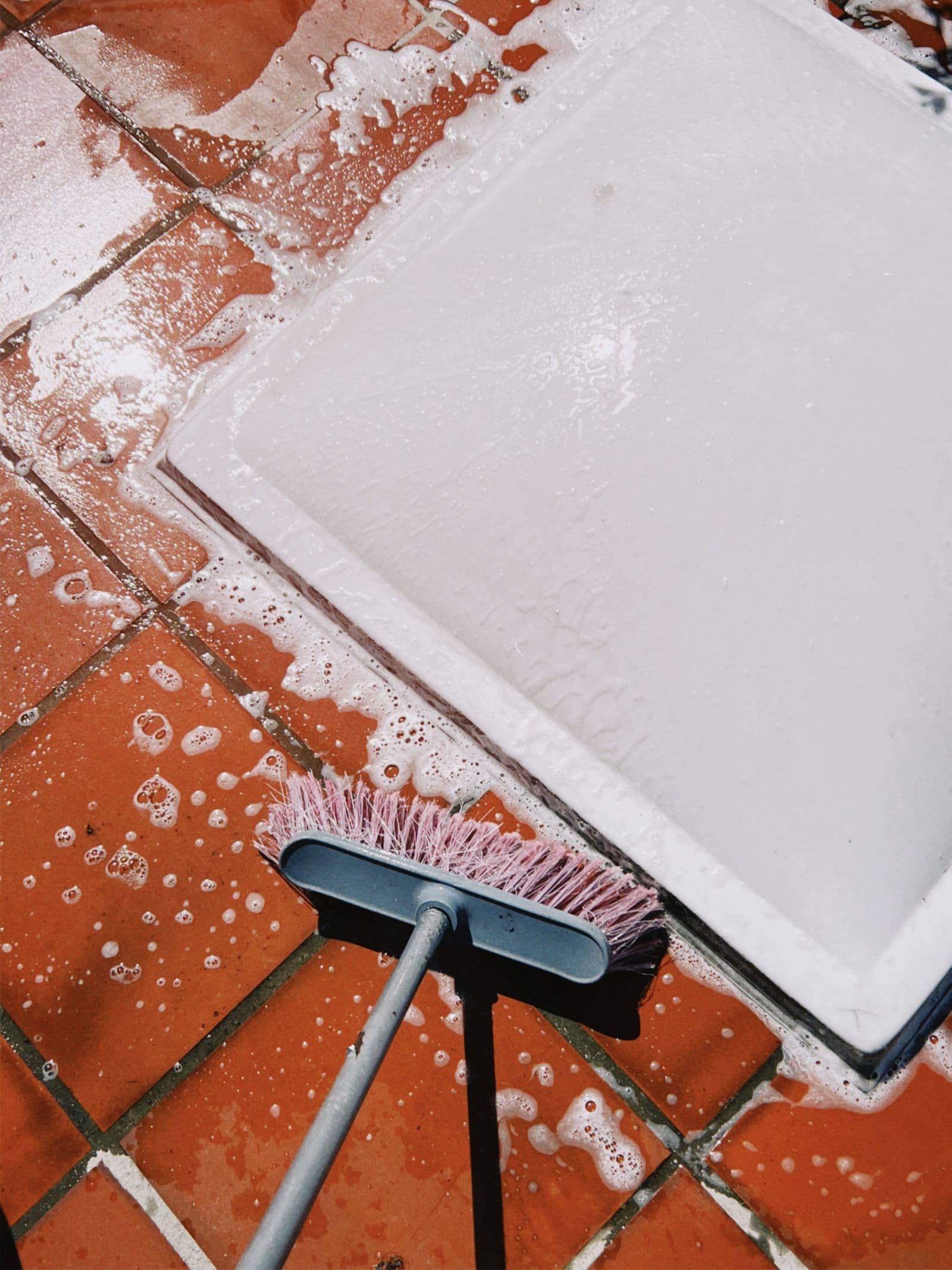 Close-up of a brush scrubbing soapy tile and grout